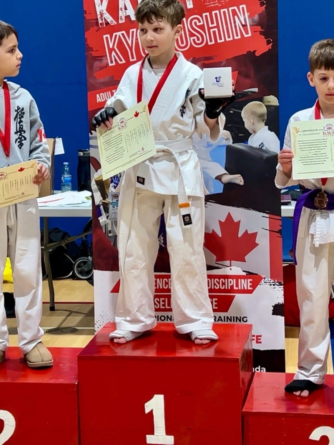 A young Winterpeg Dojo student on the first place podium holding his certificate and medal